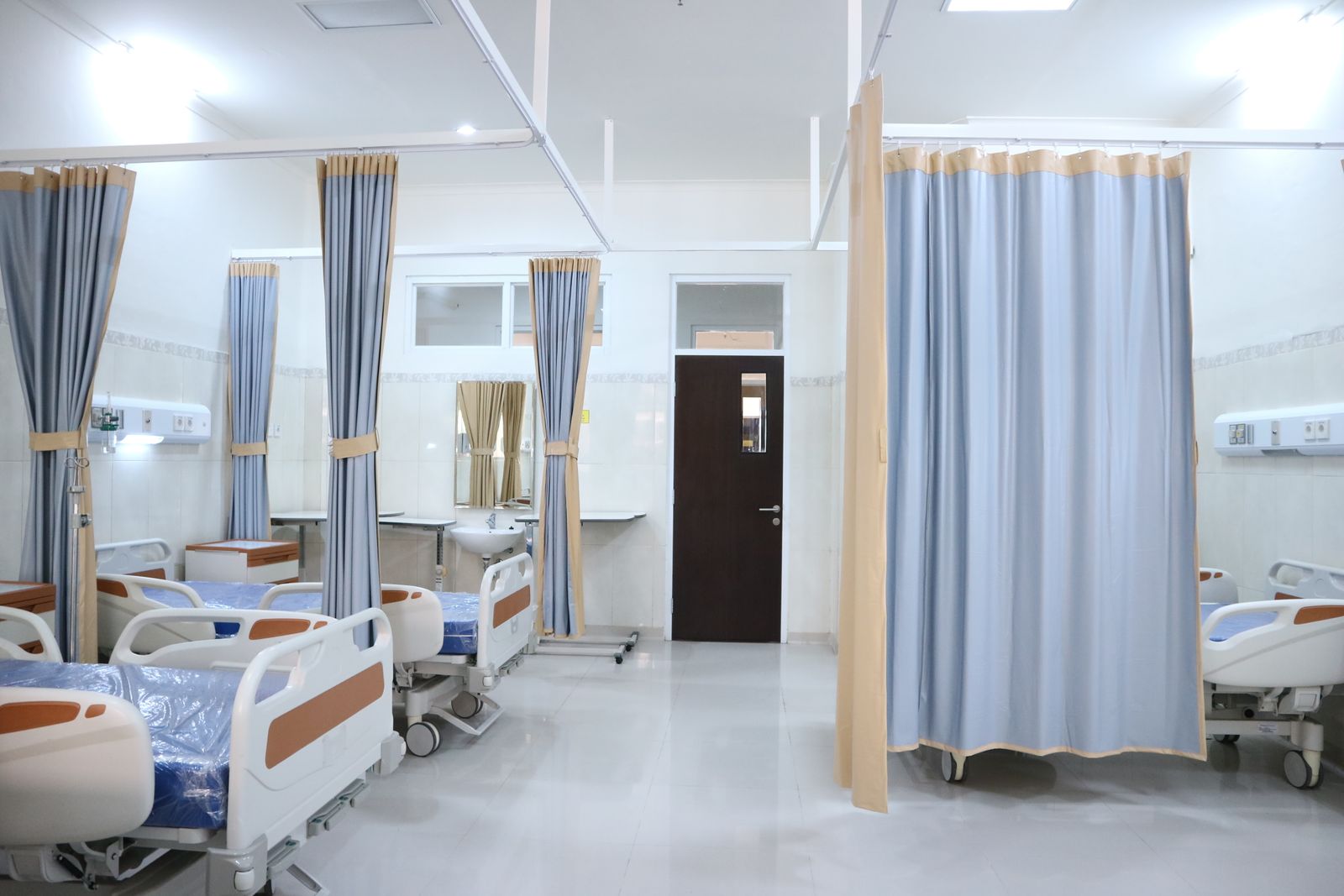 Helle Krankenstation mit mehreren Patientenbetten und medizinischer Ausstattung